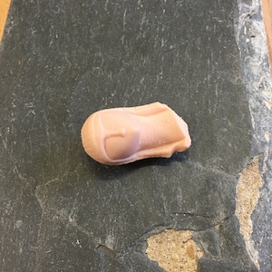 May include: A light pink, slightly misshapen, candy shaped like a rocket ship.