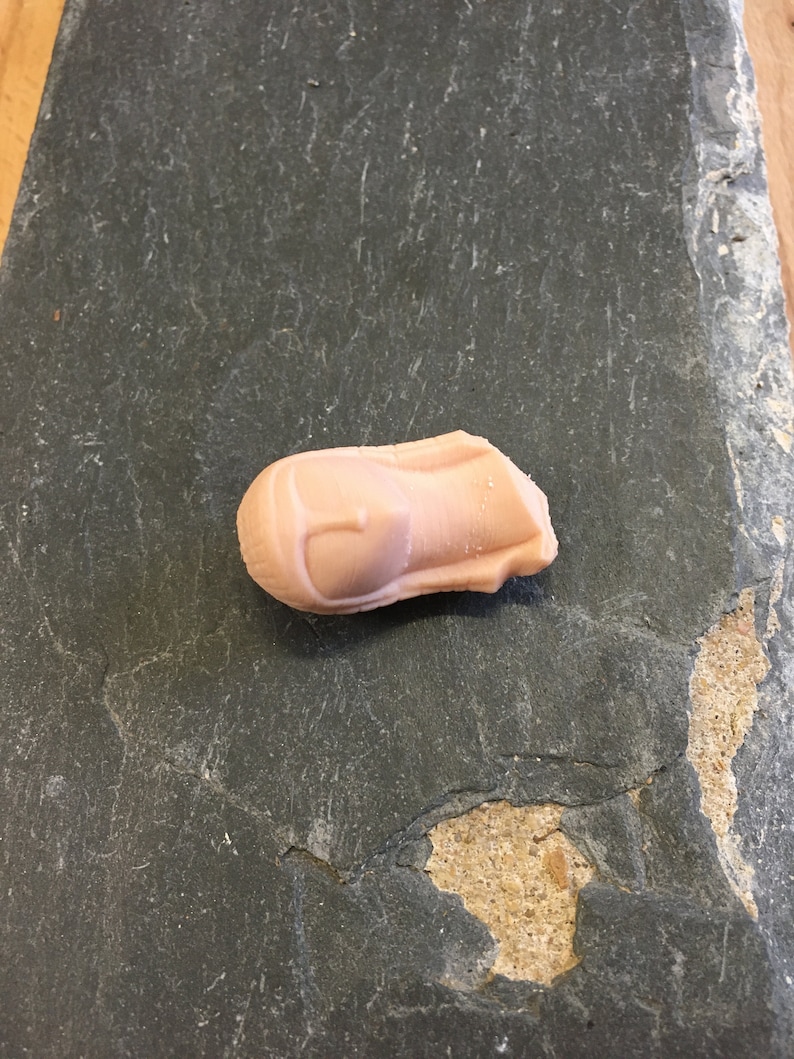 May include: A light pink, slightly misshapen, candy shaped like a rocket ship.