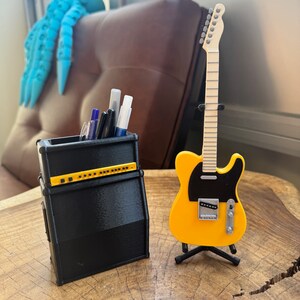 May include: A black and yellow guitar amplifier pencil holder with a yellow electric guitar on a stand.