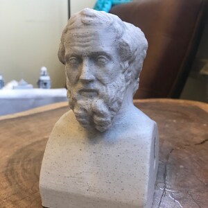 May include: A gray 3D printed bust of a man with a beard. The bust is sitting on a wooden surface.