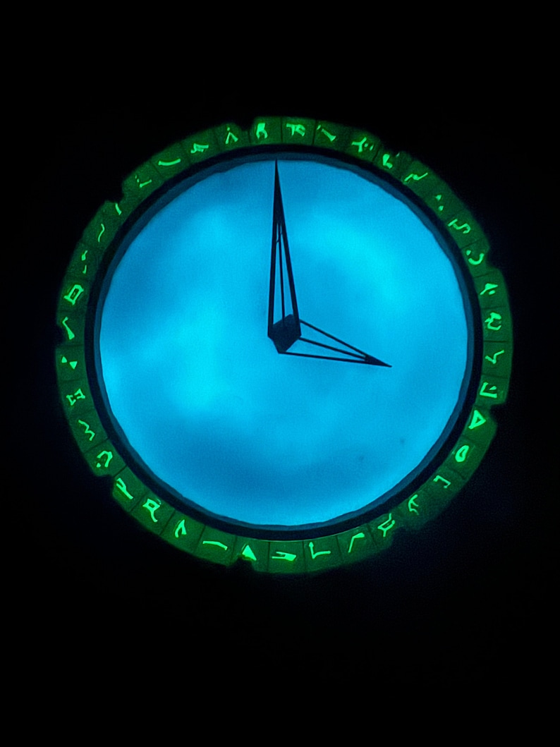 May include: A glowing blue clock with green markings around the edge. The clock face is illuminated with a blue light, and the hands are black.