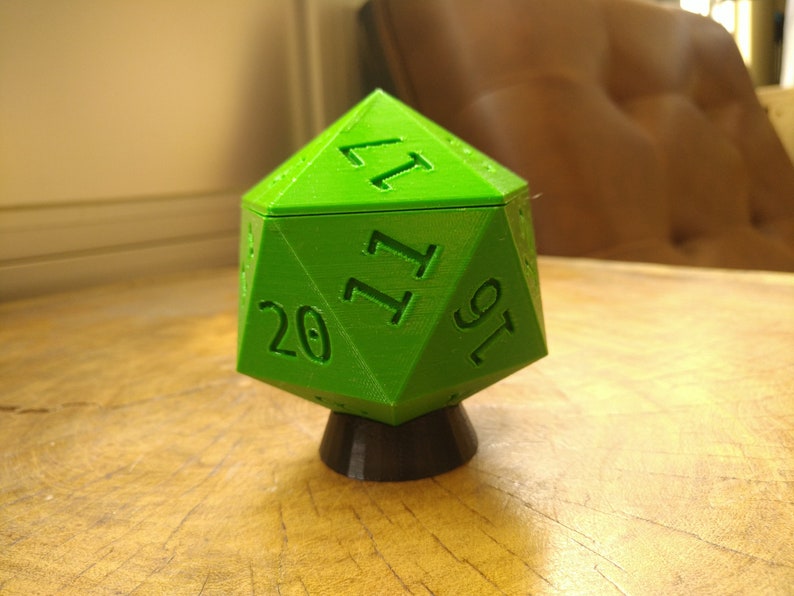 May include: A bright green 20-sided die with black numbers, resting on a black base. The die is a geometric shape with many sides and is a common tool used in tabletop role-playing games.