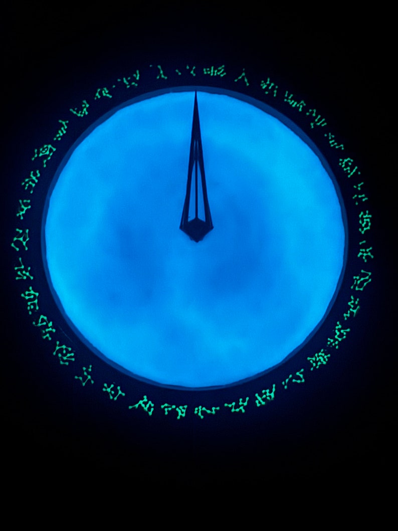 May include: A blue circular clock face with a black, triangular hand pointing to the top. The clock face is surrounded by a black ring with green glowing symbols.