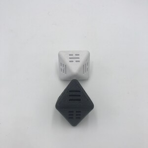 May include: Two geometric dice, one white and one black, with a pattern of lines on each face. The dice are made of a textured material.