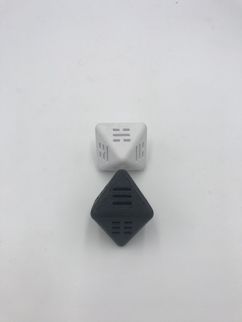 May include: Two geometric dice, one white and one black, with a pattern of lines on each face. The dice are made of a textured material.