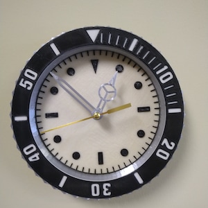 Puede incluir: Un reloj anal&oacute;gico blanco y negro con una esfera blanca y agujas negras. El reloj tiene un bisel negro con n&uacute;meros blancos alrededor del borde. Los n&uacute;meros son 10, 20, 30, 40 y 50.