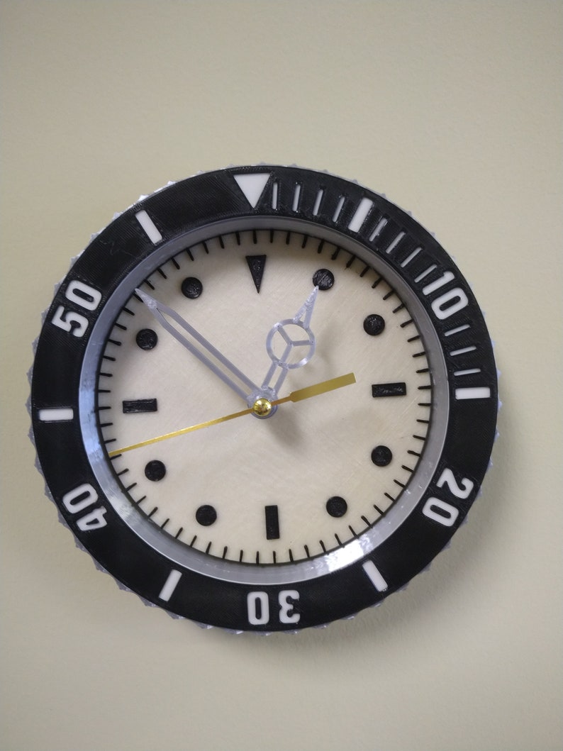 Puede incluir: Un reloj anal&oacute;gico blanco y negro con una esfera blanca y agujas negras. El reloj tiene un bisel negro con n&uacute;meros blancos alrededor del borde. Los n&uacute;meros son 10, 20, 30, 40 y 50.