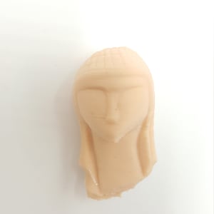 May include: A beige ceramic sculpture of a woman's head with a simple, stylized design.