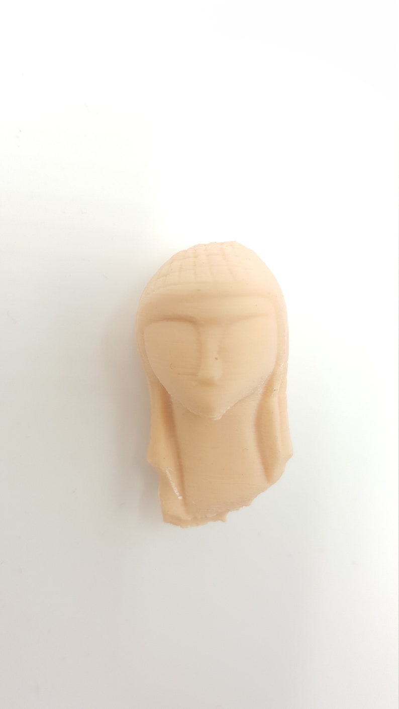 May include: A beige ceramic sculpture of a woman's head with a simple, stylized design.