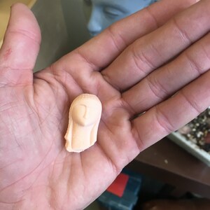 Może przedstawiać: Mała, różowa ceramiczna figurka głowy kobiety z długimi włosami.