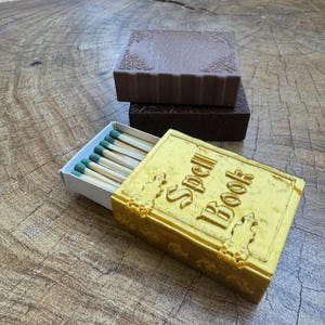 May include: A yellow matchbox shaped like a book with the text "Spell Book" on the cover. The matchbox is open and contains a row of matches with green tips.