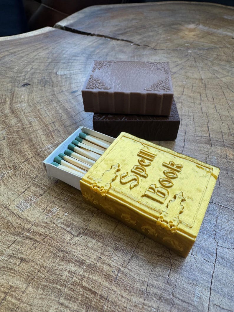 May include: A yellow matchbox shaped like a book with the text "Spell Book" on the cover. The matchbox is open and contains a row of matches with green tips.