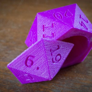May include: A purple, six-sided dice with the numbers 1, 2, 3, 4, 5, and 6 printed on the sides. The dice is open, revealing the inside of the dice.