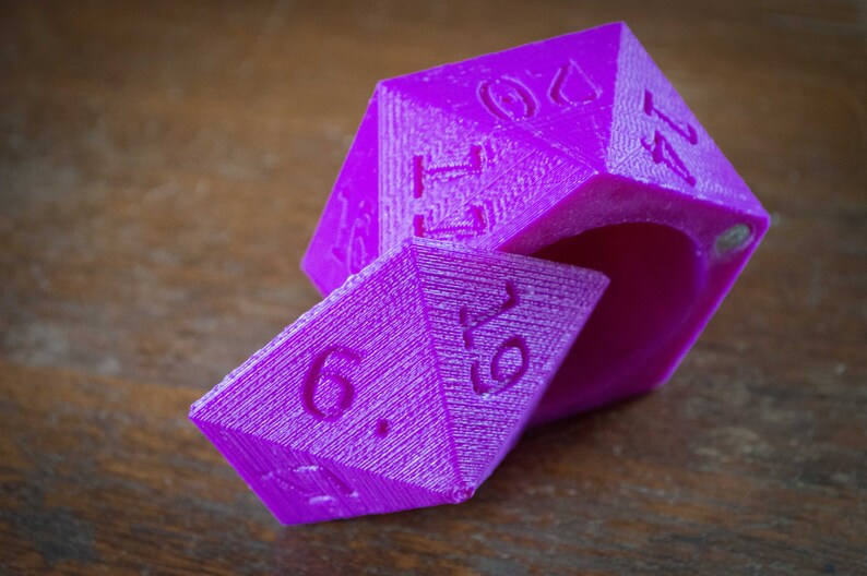 May include: A purple, six-sided dice with the numbers 1, 2, 3, 4, 5, and 6 printed on the sides. The dice is open, revealing the inside of the dice.