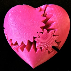 May include: A pink heart-shaped object made of interlocking gears. The gears are all different sizes and shapes, and they are arranged in a way that creates a complex and intricate design.