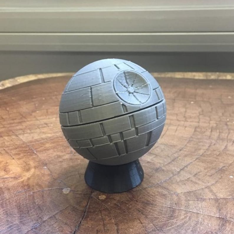 May include: A gray 3D printed Death Star model with a detailed surface and a small base.