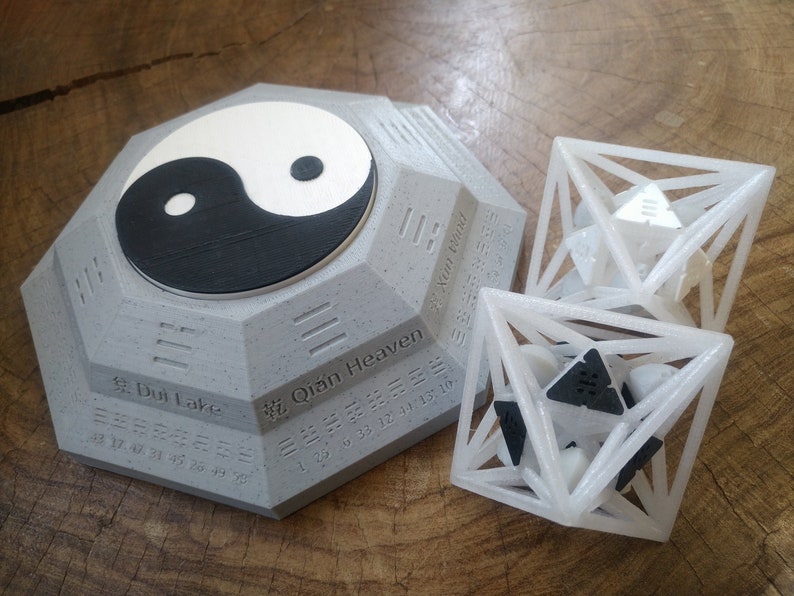 May include: A gray octagonal base with a yin yang symbol on top and the text "Dui Lake" and "Qian Heaven" in Chinese characters. Two white geometric shapes with black accents are in the foreground.