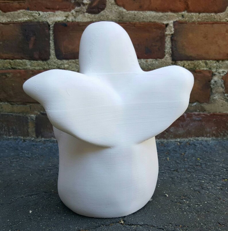K&ouml;nnte beinhalten: Wei&szlig;e Keramik-Geisterfigur mit einer glatten, abgerundeten Form und einem fl&uuml;gelartigen Design auf der R&uuml;ckseite. Der Geist steht auf einer dunklen Oberfl&auml;che.