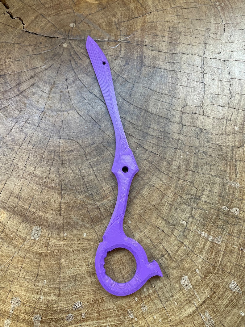 May include: A purple plastic tool with a ring on the bottom and a pointed end. The tool is designed to open packages and other items.