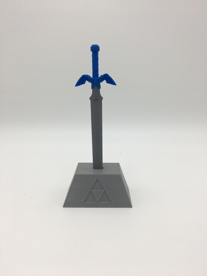 May include: A gray plastic stand with a triangular design and a blue plastic sword with a handle and wings. The sword is inserted into the stand.