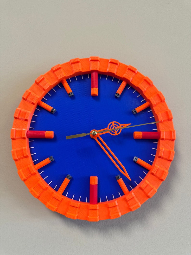 Puede incluir: Un reloj redondo naranja con una esfera azul y marcadores de hora naranja. Las manecillas del reloj son doradas y negras.