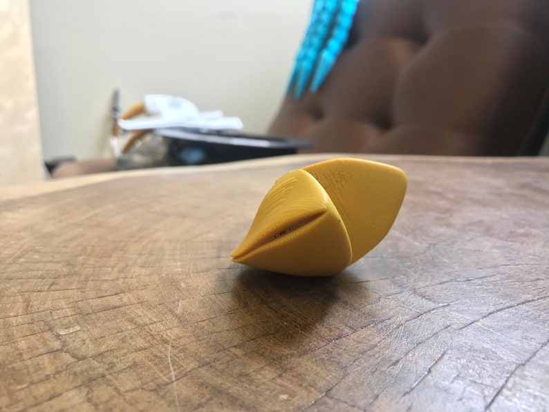 May include: A yellow, 3D printed, geometric shape with a pointed tip. The shape is lying on a wooden surface.