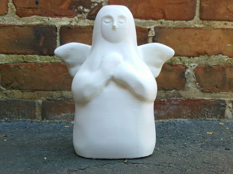 K&ouml;nnte beinhalten: Wei&szlig;e Keramik-Engelfigur mit Fl&uuml;geln und ineinander verschr&auml;nkten H&auml;nden zum Gebet. Der Engel hat ein einfaches, stilisiertes Gesicht.