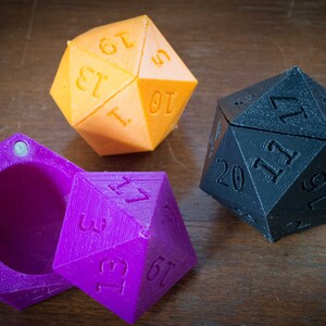 May include: Three 20-sided dice, one orange, one purple, and one black. The purple die is open, revealing an empty interior.