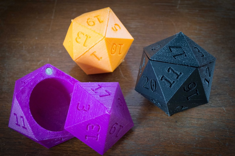 May include: Three 20-sided dice, one orange, one purple, and one black. The purple die is open, revealing an empty interior.