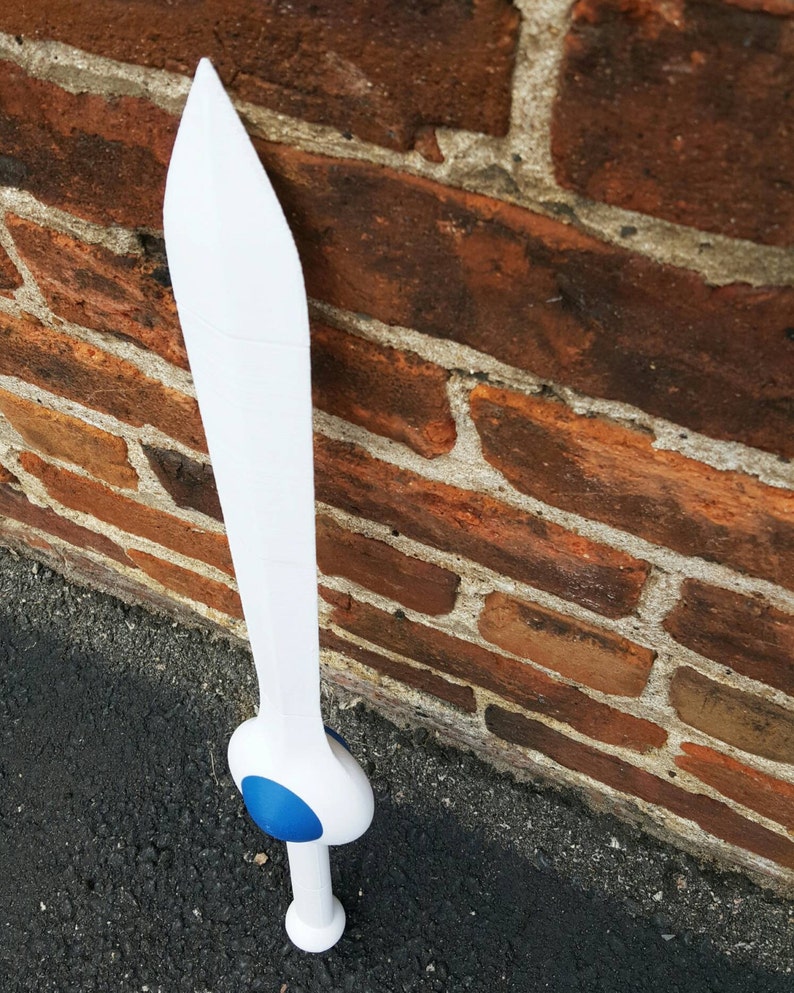 May include: A white plastic sword with a blue pommel. The sword is leaning against a brick wall.
