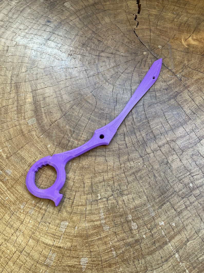 May include: A purple plastic sword with a circular handle and a sharp point. The sword is lying on a wooden surface.