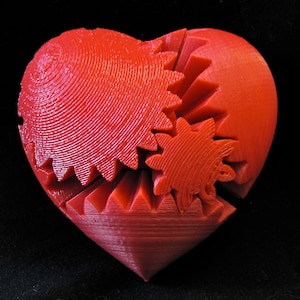 May include: A red heart-shaped object made of plastic with interlocking gears. The gears are visible on the surface of the heart.