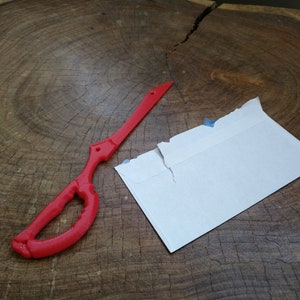May include: A red plastic replica of a sword, with a white envelope on a wooden surface.