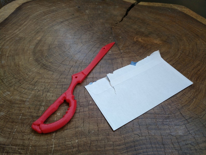 May include: A red plastic replica of a sword, with a white envelope on a wooden surface.