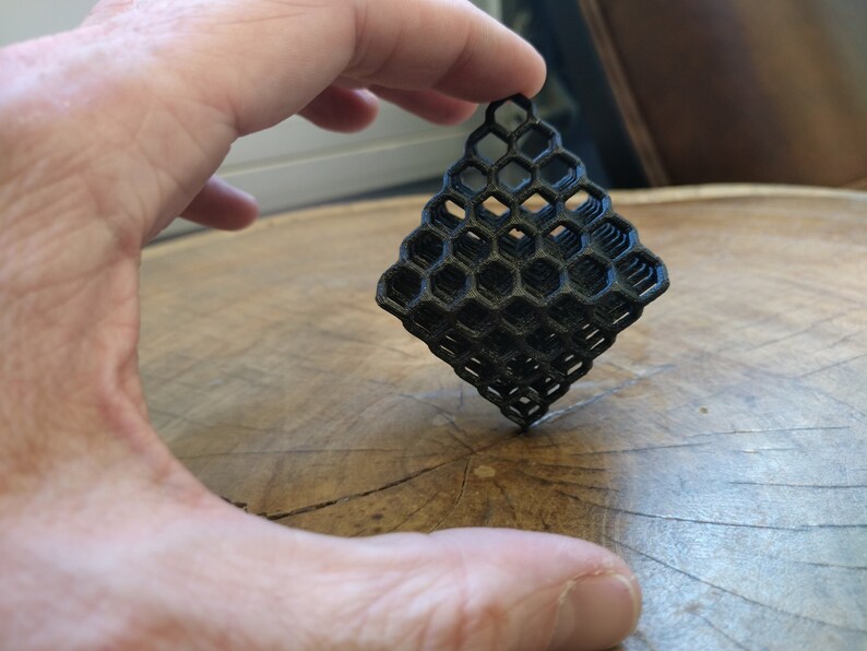 Puede incluir: Un objeto geom&eacute;trico de color negro impreso en 3D con un patr&oacute;n de panal de abeja. El objeto tiene forma de diamante y est&aacute; formado por varias capas.