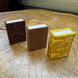 May include: Three small, decorative boxes with a book-like design. The boxes are brown, dark brown, and gold. The gold box has the words "Spell Book" printed on the front.