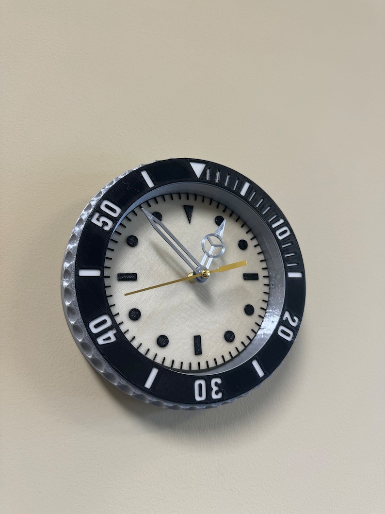 Puede incluir: Un reloj de pared negro y plateado con una esfera blanca y marcas negras. El reloj tiene un bisel grande con los n&uacute;meros 10, 20, 30, 40 y 50 alrededor del borde.