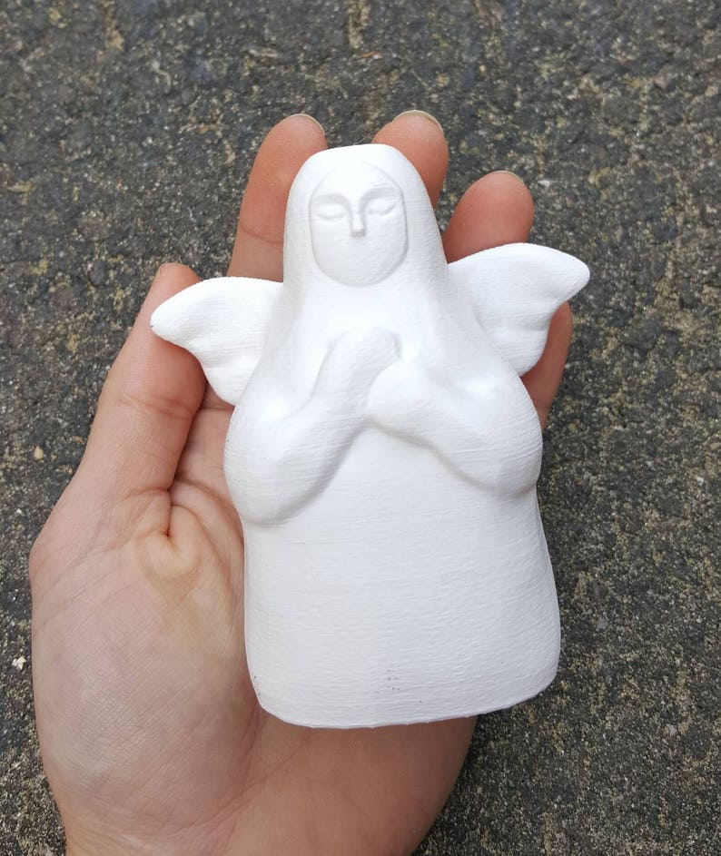 May include: White ceramic angel figurine with closed eyes and hands clasped in prayer. The angel has a simple, minimalist design.