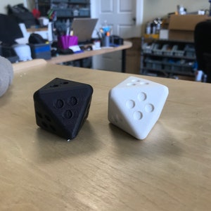 May include: Two dice, one black and one white, are shown on a wooden surface. The dice are both in a standard six-sided shape.