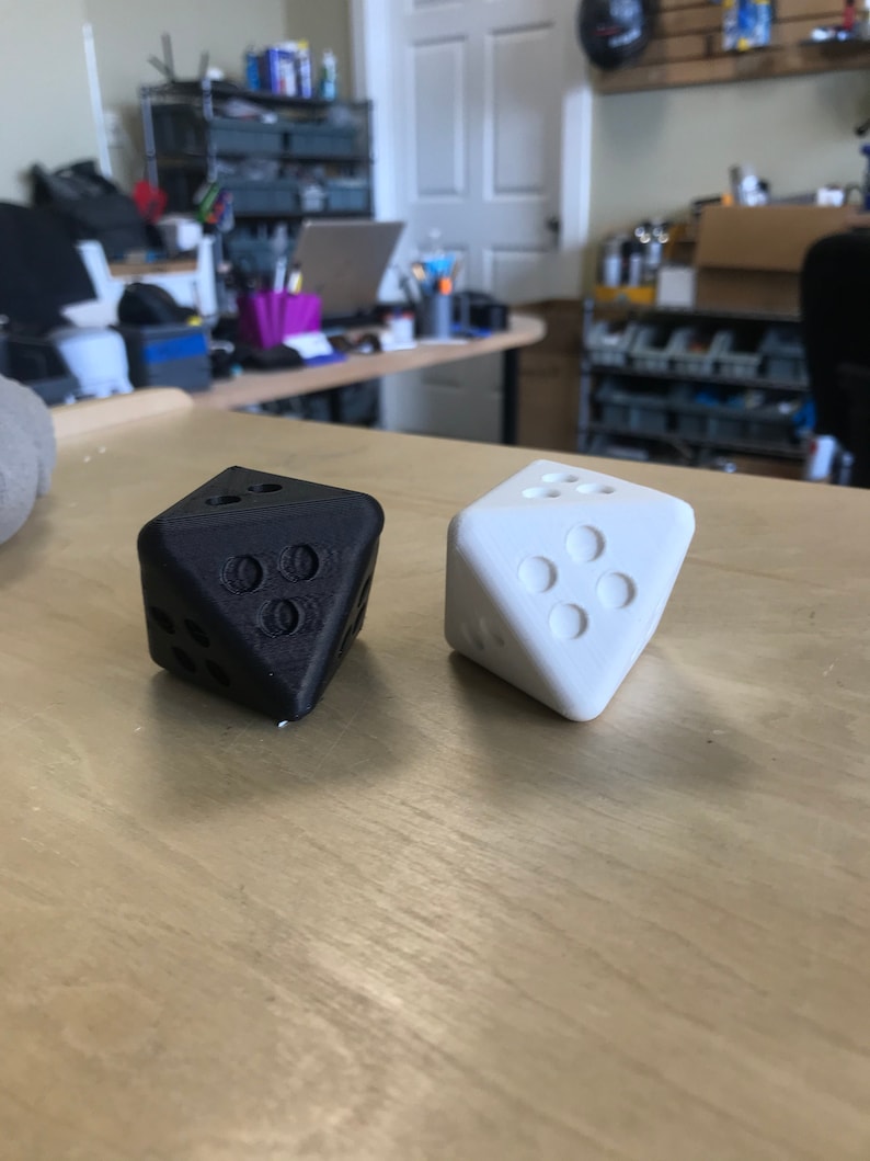 May include: Two dice, one black and one white, are shown on a wooden surface. The dice are both in a standard six-sided shape.