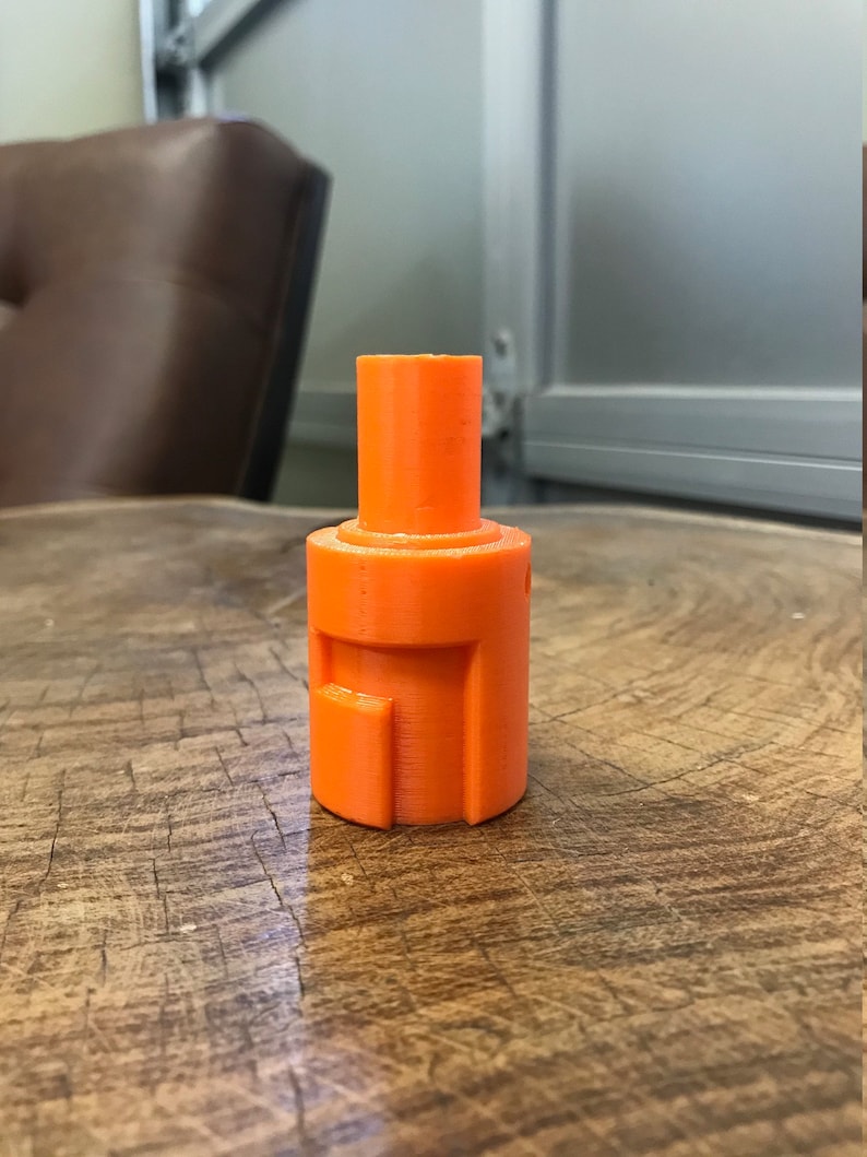 May include: An orange plastic 3D printed object with a cylindrical shape and a square opening on the side.