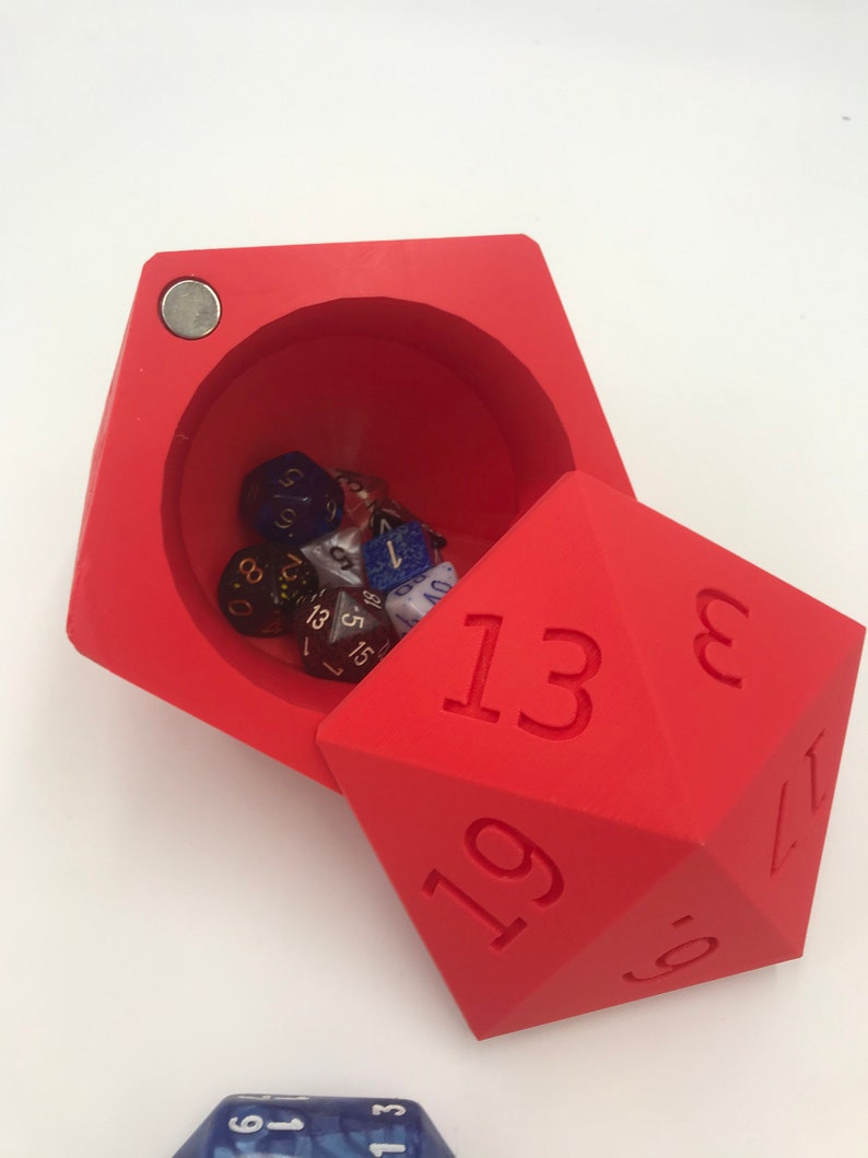 May include: Red dice tower with a lid that opens to reveal a compartment filled with various colored dice. The dice tower has the numbers 13, 19, 8, 17, and 5 printed on its sides.