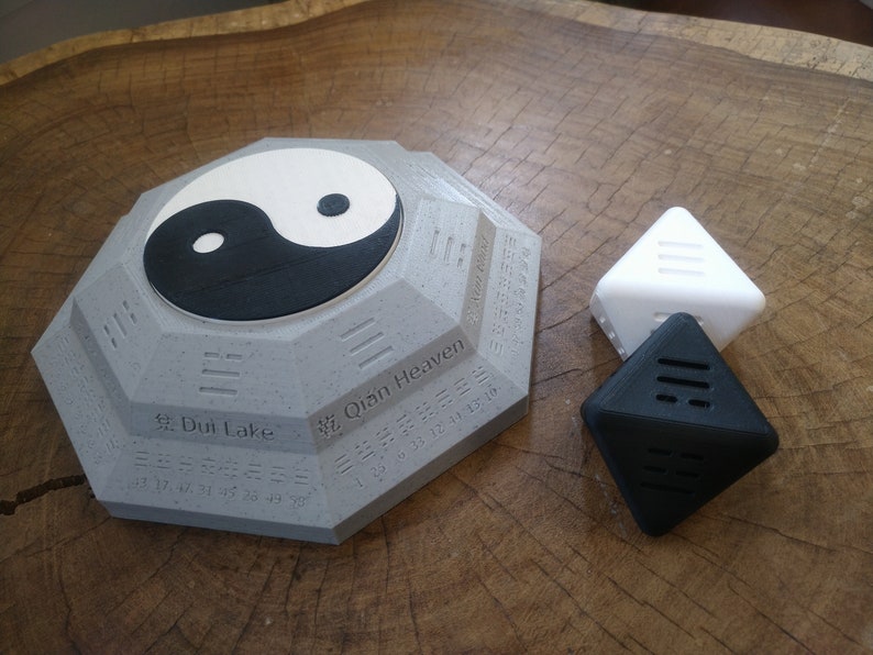 May include: A gray octagonal base with a yin yang symbol on top. The base has Chinese characters and numbers around the edge. There are two triangular pieces, one white and one black, with lines on them.