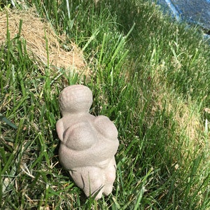 Puede incluir: Una escultura de piedra gris de una persona sentada con las piernas cruzadas. La escultura est&aacute; en un &aacute;rea cubierta de hierba.