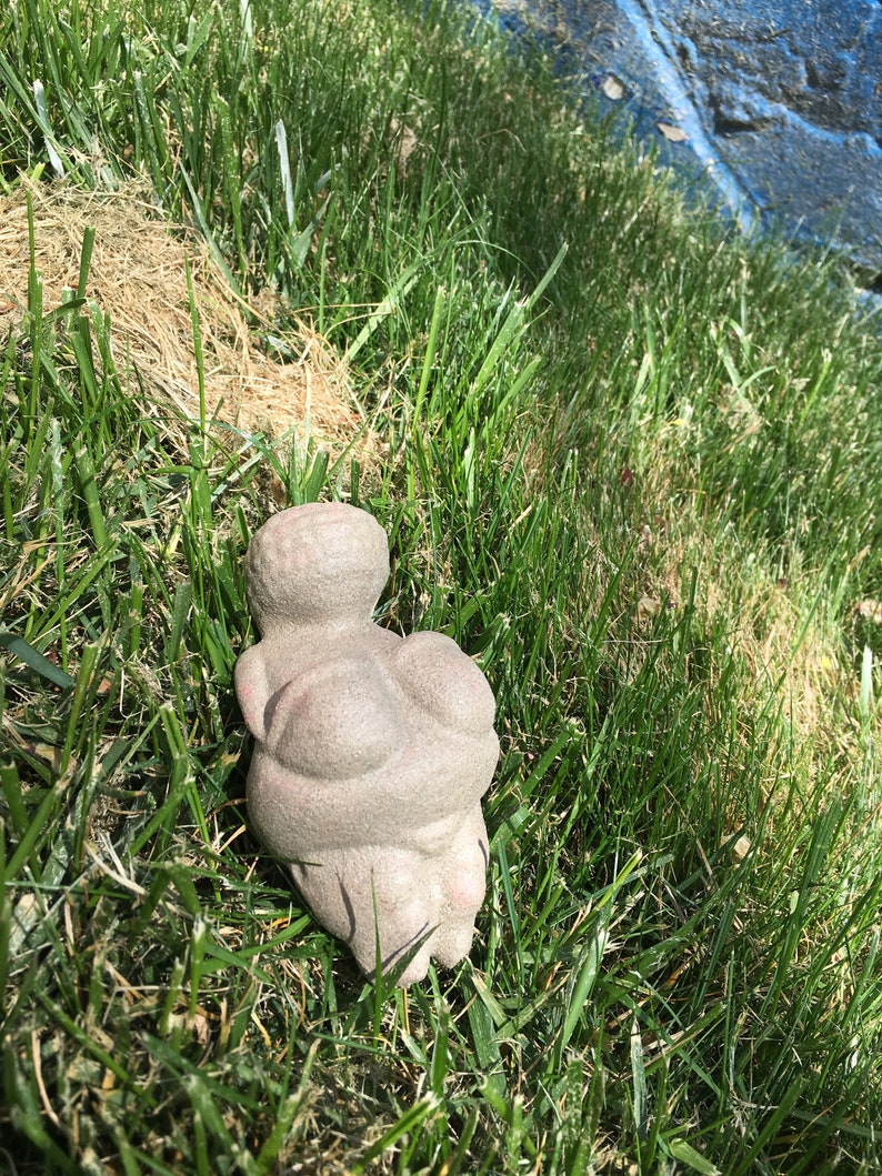 Puede incluir: Una escultura de piedra gris de una persona sentada con las piernas cruzadas. La escultura est&aacute; en un &aacute;rea cubierta de hierba.