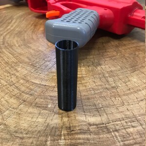 Peut inclure: Un jouet pistolet rouge et gris avec une extension de canon en plastique noir. Le pistolet est sur une surface en bois.