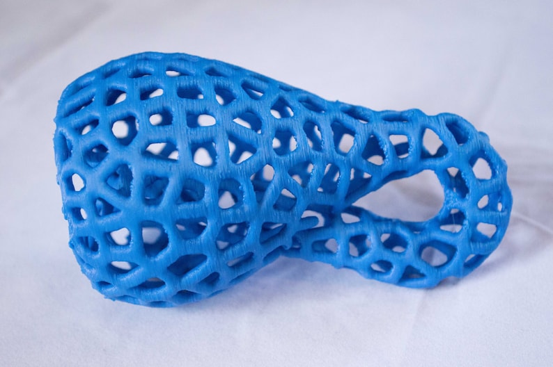 May include: A blue 3D printed object with a lattice design. The object is shaped like a long, thin oval with a hole in the middle.