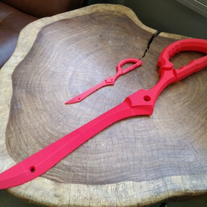 May include: Two red plastic prop swords, one large and one small, are displayed on a wooden surface. The larger sword is shaped like a pair of scissors.