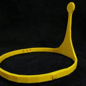 May include: A yellow plastic headband with a single point extending upwards. The headband has a series of small holes along the top.