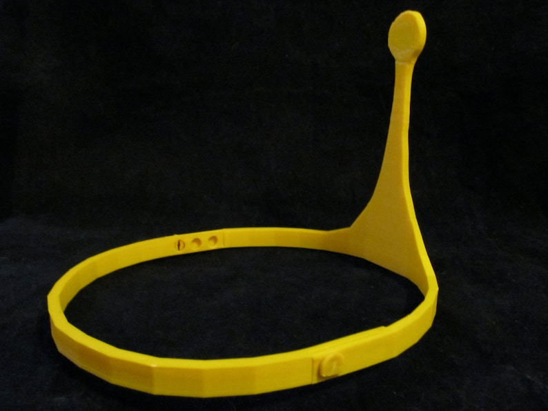 May include: A yellow plastic headband with a single point extending upwards. The headband has a series of small holes along the top.